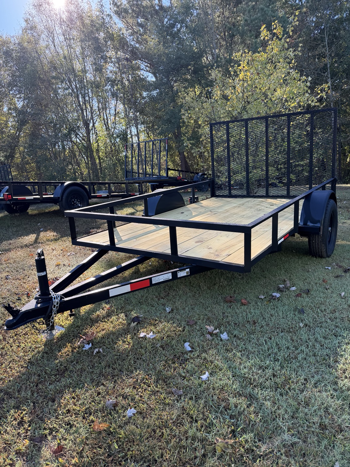 Black 6.5 by 10 foot single axle utility trailer with wood deck and mesh ramp gate